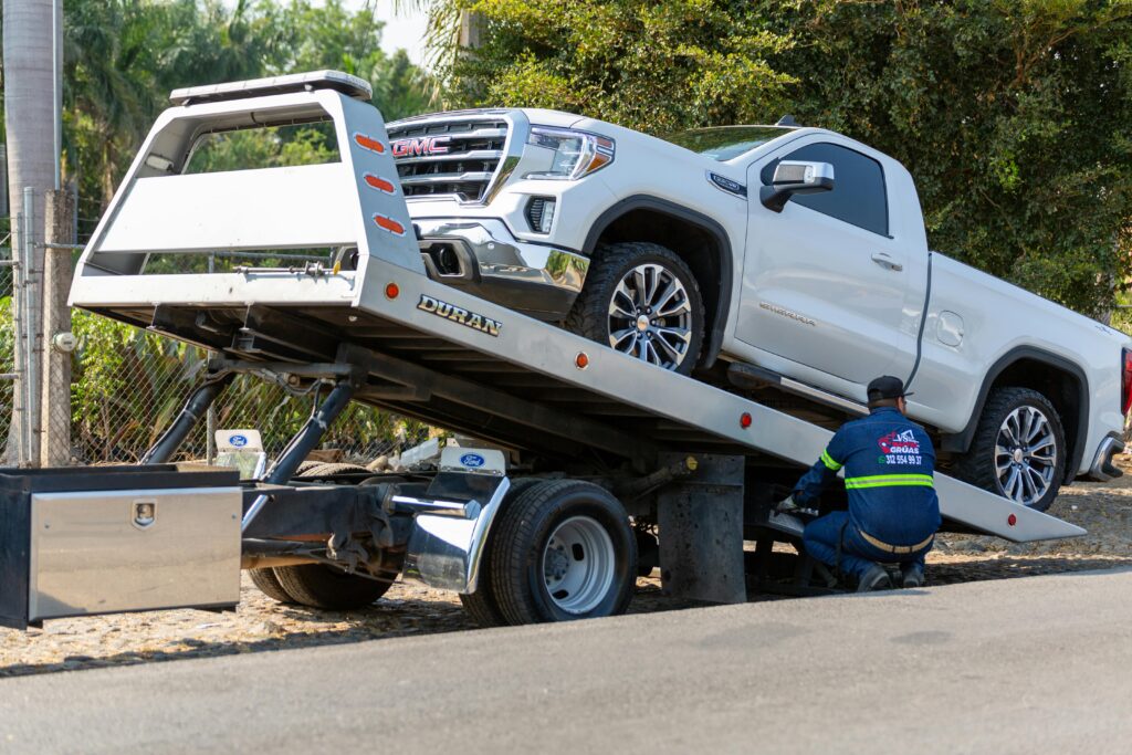pexels-photo-17429097-17429097 Tow truck operator loading white GMC pickup truck on street in daytime.